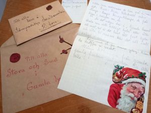 Pöydällä vanhoja kirjekuoria, joihin on kiinnitetty vahasinettejä. Vahalla on myös kiinnitetty kuusenoksia. Kirjeeseen on laitettu isokokoinen värikäs kohokuvioinen tarra joulupukista