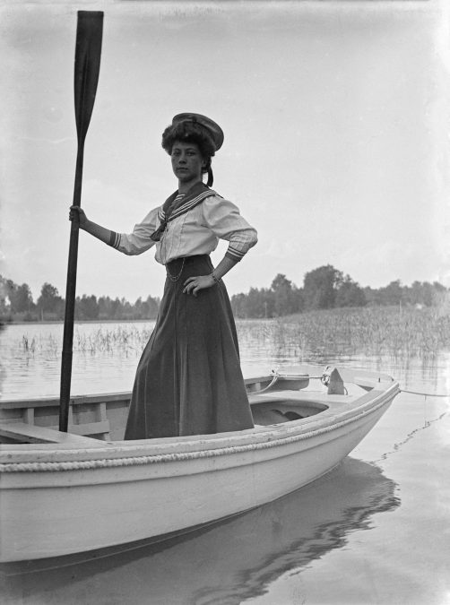 Margit Nyberg merimiesasu päällä soutuveneessä ja airo kädessä Meilahdessa 1900-luvun alussa.